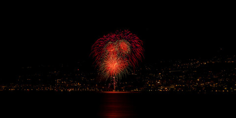 Long exposure of colorful fireworks reflecting in the water above a city in night lights © Hervé Maniraguha/Wirestock Creators