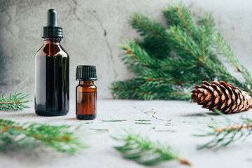 Front view of glass bottles of  pine essential oil with fresh fir tree branch over gray background...