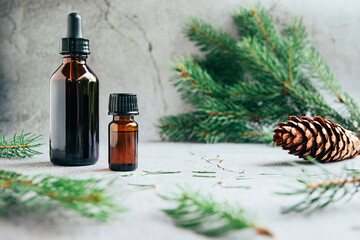 Fototapeta premium Front view of glass bottles of pine essential oil with fresh fir tree branch over gray background aromatherapy concept.