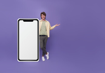 Young handsome man standing with mockup big Smartphone blank white screen isolated on purple studio background.