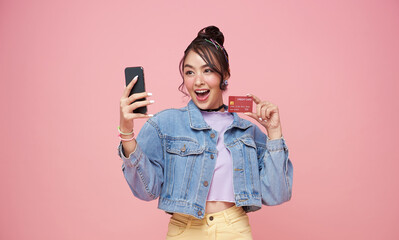 happy young asian woman using mobile phone and credit card isolated over ping background. - obrazy, fototapety, plakaty