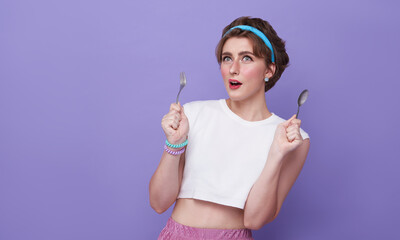 beautiful young woman holding spoon and fork ready to eat isolated on purple background.