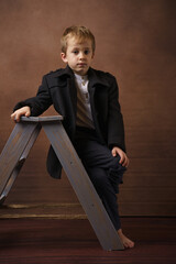 Portrait of a little boy smartly dressed sitting on a footstool. Retro style.