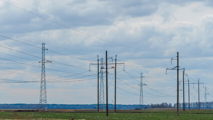 High voltage post on blue sky with clouds background. Electrical net of poles on blue sky and spring meadow.
