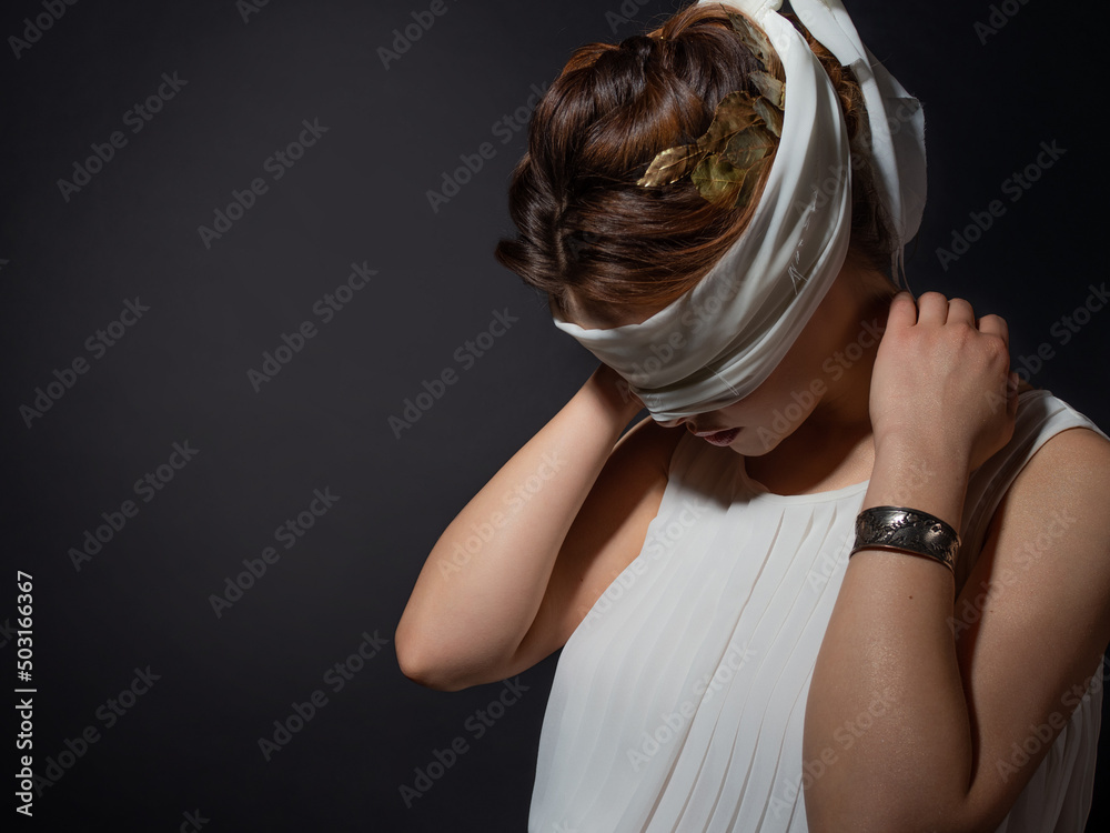 Wall mural An antique heroine blindfolded, a young woman in a tunic with a blindfold, a contrasting close-up portrait on a black background