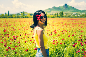 Young caucasian woman portrait stand in poppy field in springtime and smile to camera. Wellness and...