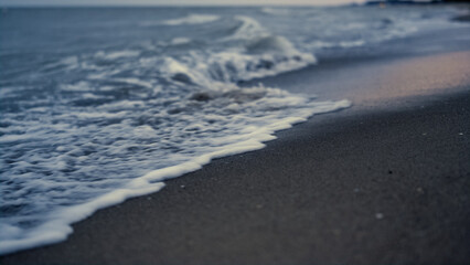 Sea wave crashing sand on sunset evening beach. Dusk ocean tide splash coastline