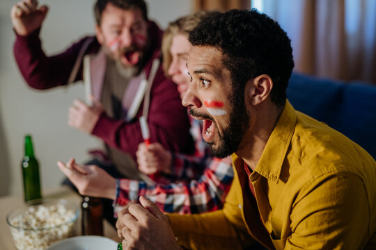 Close-up of excited football fan watching match with friends at home.