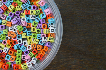 Colorful alphabet beads in a plastic bowl. Copy space for the text