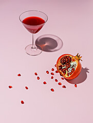 Cocktail glass and a fresh pomegranate with seeds on pastel pink background. Creative drink or food...