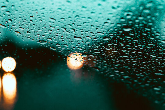 Gotas de lluvia gotitas en el vidrio parabrisas del auto con luces desenfocadas