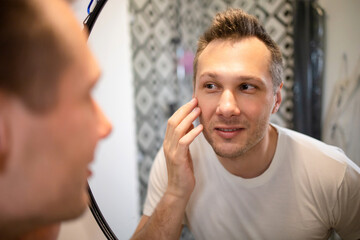 Smiling man examining his face in a bathroom mirror