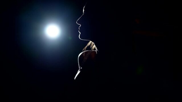 silhouette of sexy lady in darkness against bright soffit in studio, artistic contour light