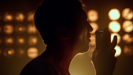 Unrecognizable man singing microphone in night club. Silhouette of guy singer.