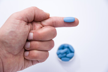 Male hand showing a blue pill on a finger and in the background container full of blue pills - 503174946