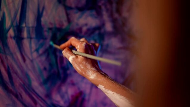 woman artist is working alone in her workshop in night, drawing abstract picture on canvas, closeup