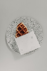 Close up of small homemade waffle served in white paper bag.