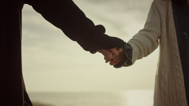 Dating lovers hold hands on sunrise sea beach nature. Couple touch arms outside.