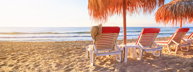 Coastal landscape, banner - view of the sandy sea beach with deck chairs and canopies. Beach holiday concept