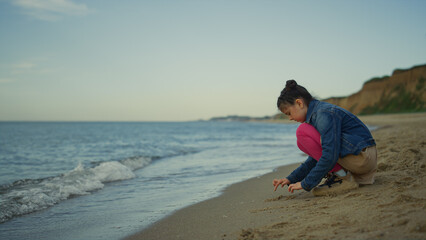 Cute girl playing sand on sea beach. Kid enjoying holiday at nature shoreline.