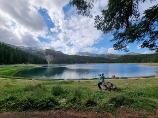 woman makes photos near a lake in the mountains. Lady sits on stone  near Blake lake in national park `durmitor` Montenegro. Unesco world heritage. Europe travel site. Vacation concept.  Tourism in ad