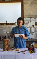 Man with a passion for DIY checks projects with his tablet in his workshop.