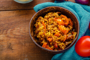 A plate of bulgur with vegetables and mushrooms on a blue napkin next to tomatoes on a wooden table.