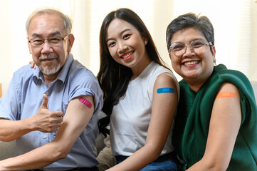 Group of diverse age Asian people family senior showing bandage plaster on arm after received covid vaccination for prevent covid-19 infection. Coronavirus pandemic protection health care concept. - obrazy, fototapety, plakaty