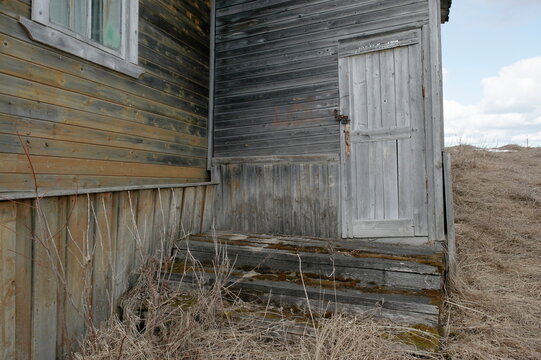 a fragment of an old abandoned house with a closed door and a porch overgrown with moss