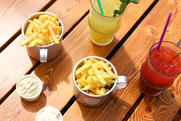Two bowls of french fries, creamy sauces and two lemonades on wooden table. Outdoor cafe, having brunch on sunny day. Fastfood, flat lay.