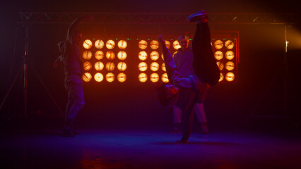Breakdance crew making tricks on dance floor. Silhouettes hip hop team on stage.