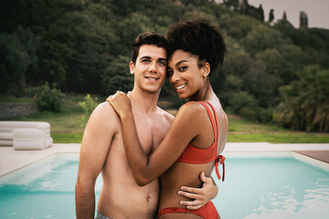 Portrait of a biracial affectionate couple of young people hugging by the swimming pool - multi-racial integration, summer vacation and lifestyle concept