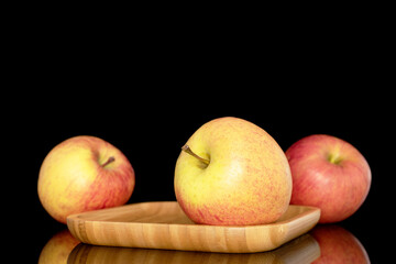 Three sweet ripe apples on a bamboo tray, close-up, isolated on a black background.