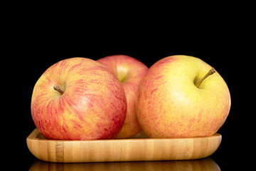 Three sweet ripe apples on a bamboo tray, close-up, isolated on a black background.