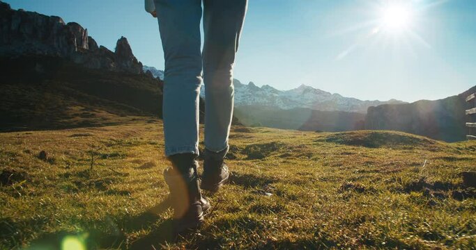 Cinematic footage of woman legs in trekking boots walks along the mountain snow peaks on background. Hiker on his journey on vacations wit epic views