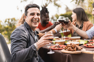 Portrait of a smiling mature man looking at the camera holding a glass of red wine - blurred in the background family friends party are toasting together -