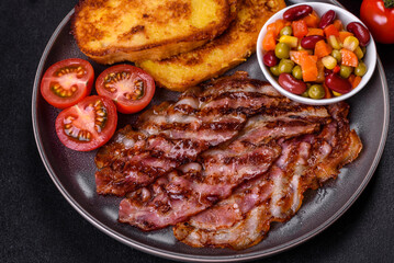 Slices of delicious grilled bacon with croutons fried in egg with spices, salt, vegetables and herbs