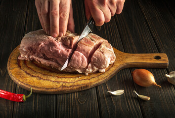 Professional chef cuts meat with a knife before baking. Spices on the kitchen table in a restaurant for preparing a delicious lunch or dinner