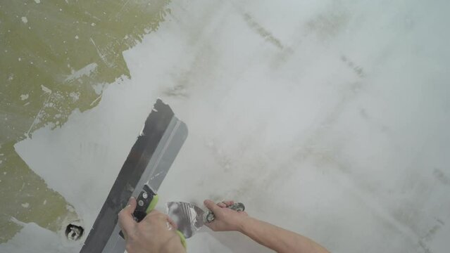 The process of puttying the ceiling with a spatula. Man with a spatula and putty, applies mastic to the ceiling to level the surface. Ceiling renovation concept.