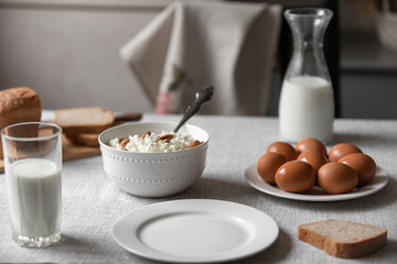 At home, in the kitchen, the table is covered with a linen tablecloth and there are natural and healthy products, milk and cottage cheese, bread and boiled chicken eggs on it
