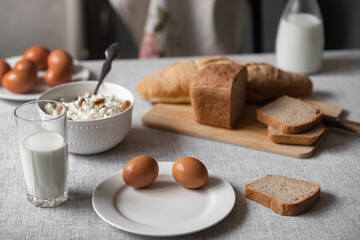 the table is covered with a linen tablecloth and there are natural and healthy products, milk and cottage cheese, bread and boiled chicken eggs on it