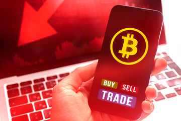 Businessman with bitcoin buy and sell trade application on mobile phone, red stock chart on laptop background photo