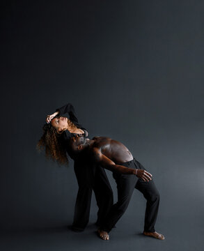 Side view of afro american man topless man and curly haires woman in suit, bending bodies back while rehearsing of dance movement in isolated black studio