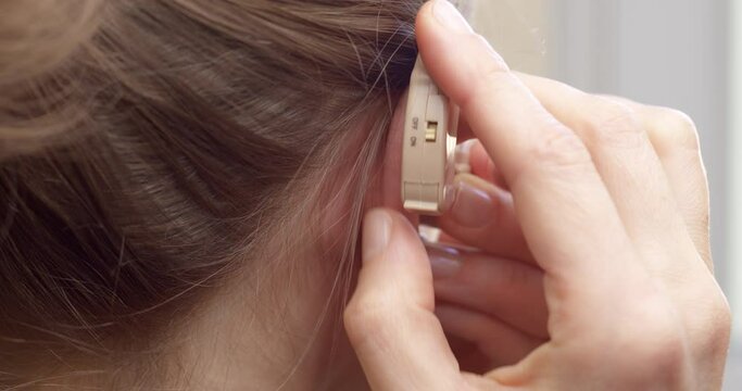 A woman uses a hearing aid on her ear. Close-up.