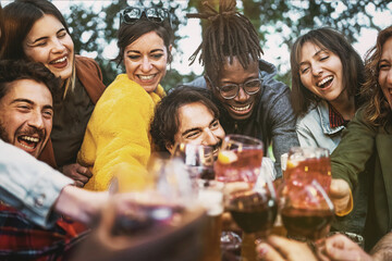 Fototapeta na wymiar Multiethnic group of excited young people having fun toasting wine and beers together at terrace birthday party - lifestyle concept of multigenerational diverse family stay together - focus center man
