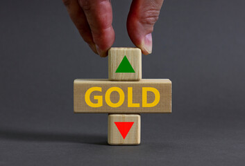 Gold price symbol. Businessman holds a wooden cube with arrow symbolizing that Gold price are going...