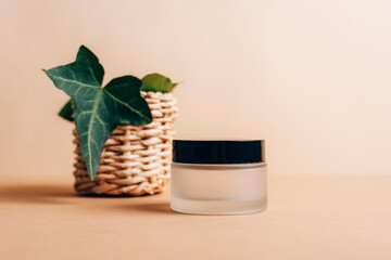 Cream jar and green leaf on beige background. Natural cosmetics, spa and wellness concept. Close up