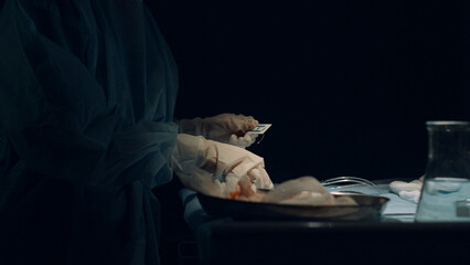 Nurse hands preparing tools for wound suturing in dark operating room closeup.