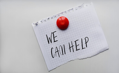 Paper note written with WE CAN HELP inscription on cork board