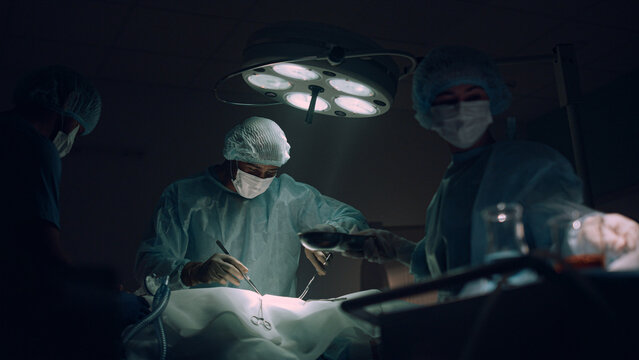 Doctors team performing surgical operation in dark hospital operating room.